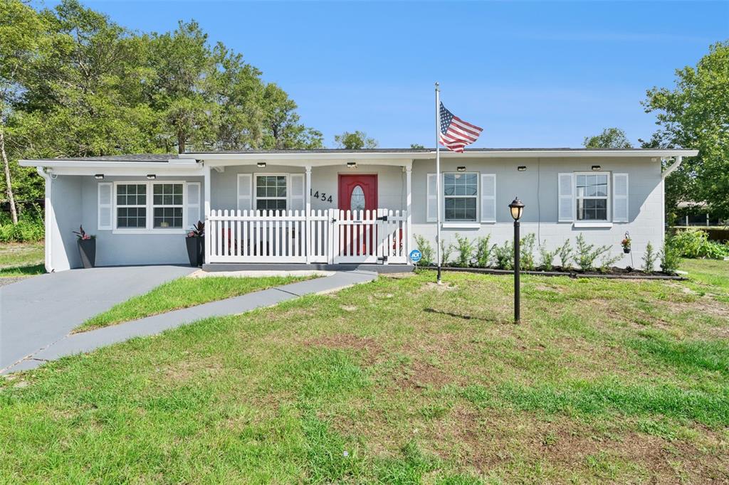 A single-story gray house with a white picket fence, red door, and American flag — 1434 DELTONA BOULEVARD, DELTONA, FL