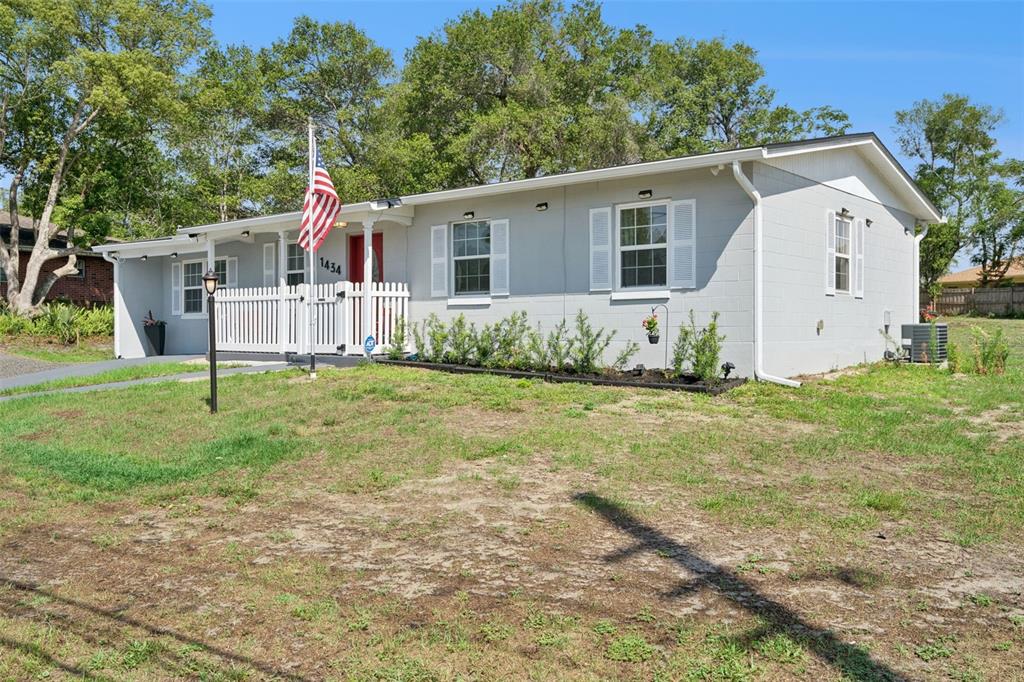 A single-story gray house with a white picket fence and an American flag — 1434 DELTONA BOULEVARD, DELTONA, FL