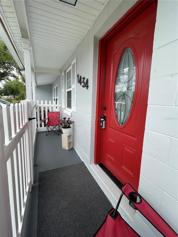 A red front door with a glass oval insert sits on a covered porch — 1434 DELTONA BOULEVARD, DELTONA, FL