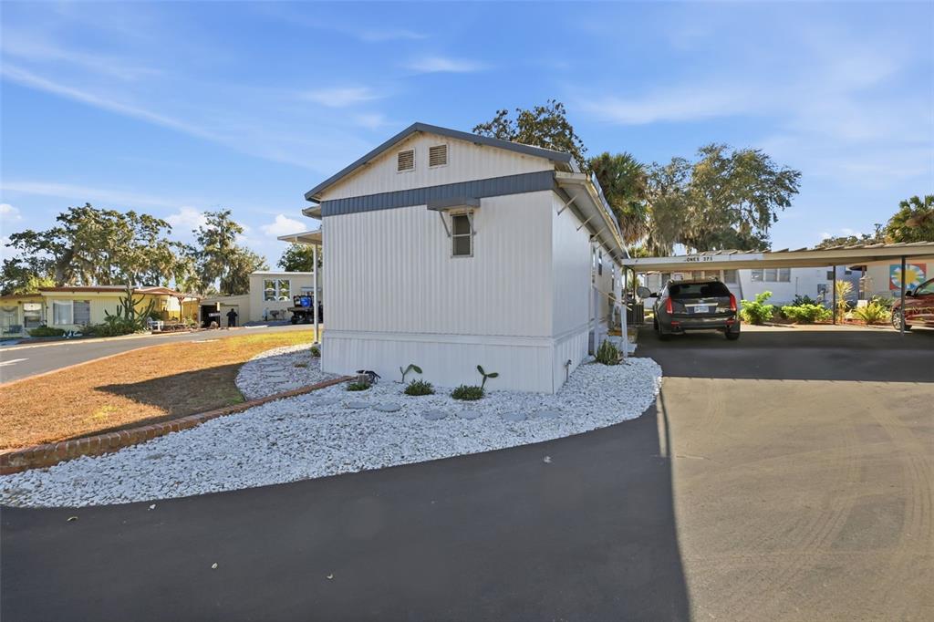 A mobile home with white siding, a carport, and a white rock garden exterior — 3896 PICCIOLA ROAD UNIT #371, FRUITLAND PARK, FL