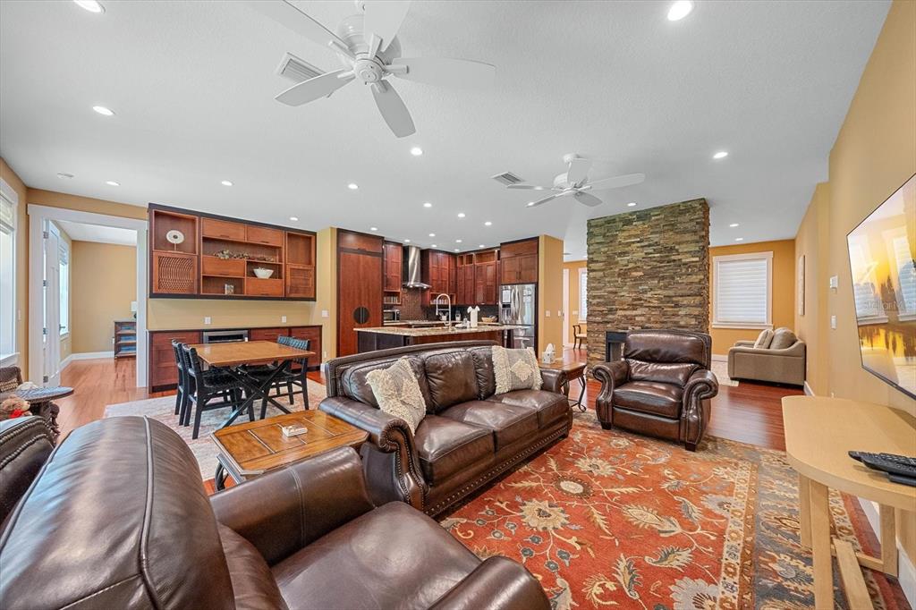 An open-concept living room features leather furniture, a stone fireplace, and a kitchen with wood cabinetry — 2395 HYDE PARK STREET, SARASOTA, FL