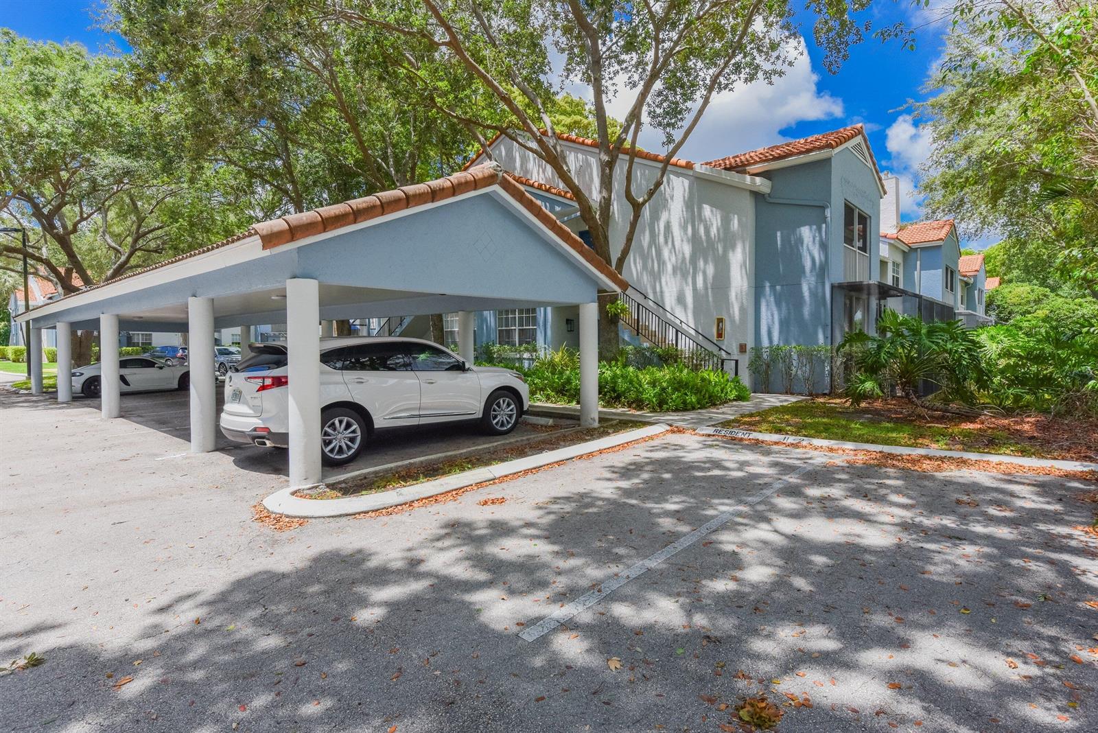 A white SUV is parked under a covered carport next to a two-story apartment building — 3131 Clint Moore Road # 208, Boca Raton FL 33496, BOCA RATON, FL