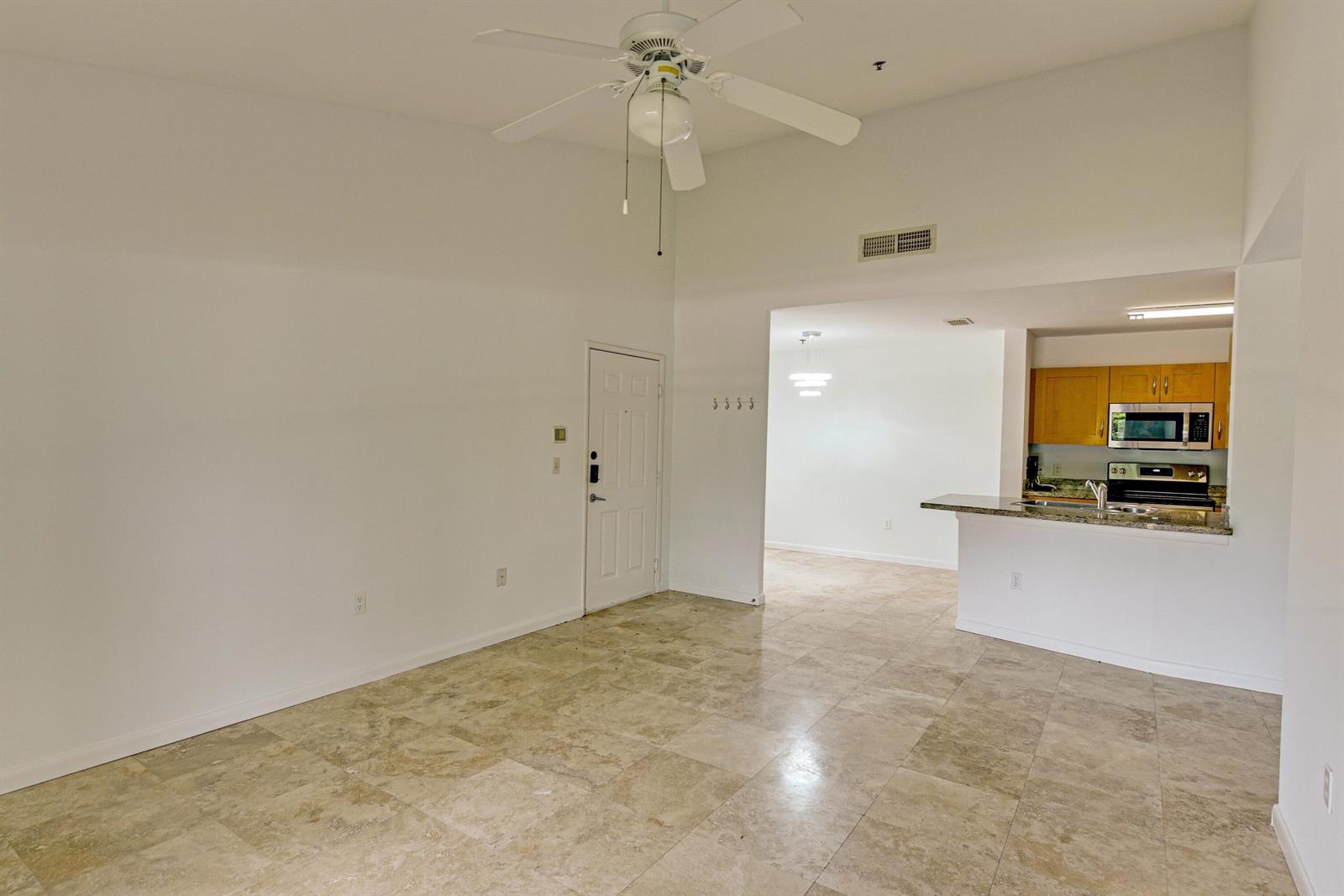 An open-concept living area features tile flooring, a ceiling fan, and an adjacent kitchen — 3131 Clint Moore Road # 208, Boca Raton FL 33496, BOCA RATON, FL