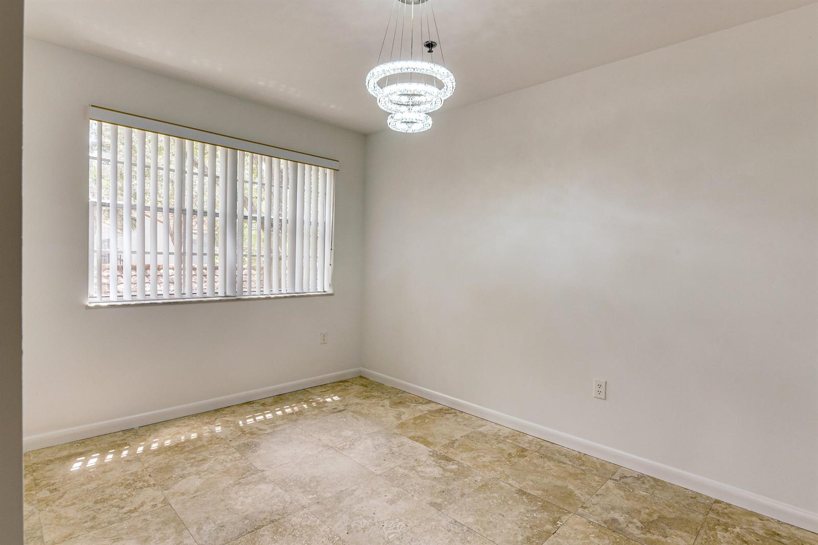 An empty dining room features a modern tiered chandelier, white walls, and beige tile flooring — 3131 Clint Moore Road # 208, Boca Raton FL 33496, BOCA RATON, FL