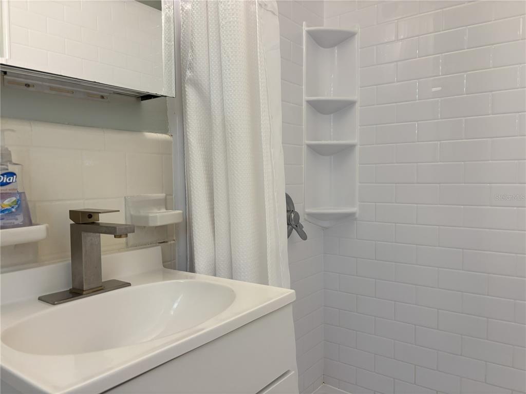 A bathroom features a white vanity with a modern faucet and a tiled shower area — 170 ROOSEVELT DRIVE UNIT 8, SARASOTA, FL