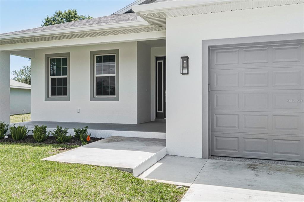 The exterior of a white house features a grey garage door and a covered porch — 141 SWAN DRIVE, ROTONDA WEST, FL