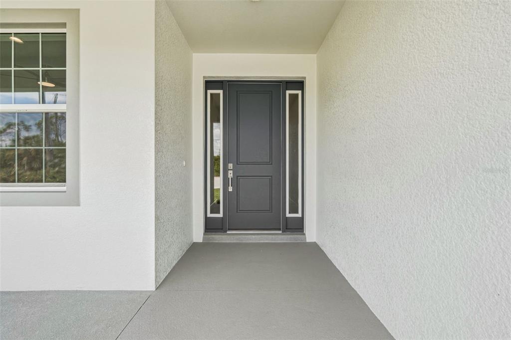 A gray front door with sidelights is centered under a covered entryway with stucco walls — 141 SWAN DRIVE, ROTONDA WEST, FL