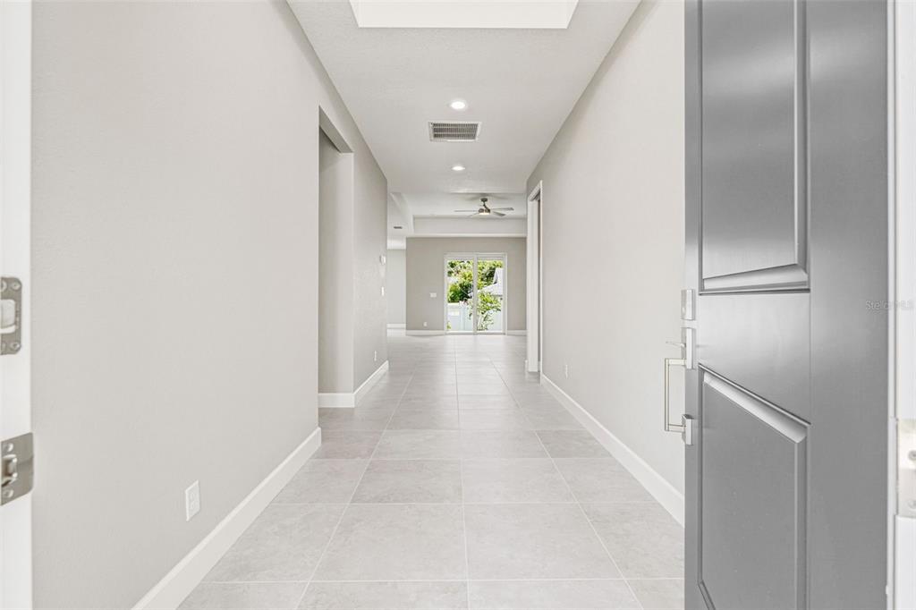 A bright hallway with light gray tile flooring leads toward a glass sliding door — 141 SWAN DRIVE, ROTONDA WEST, FL