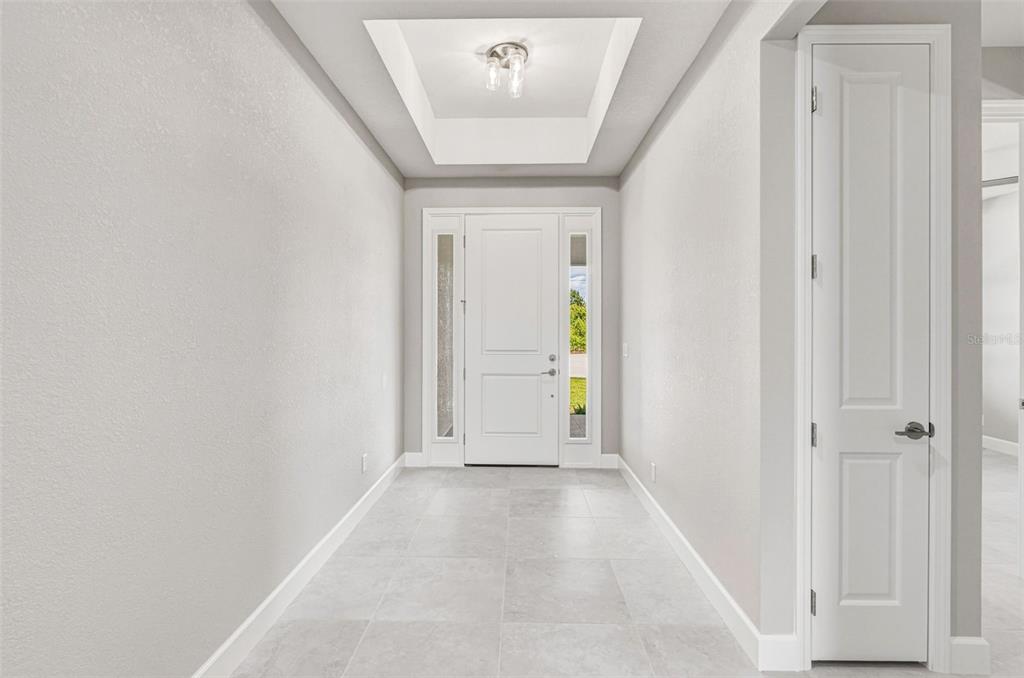 A bright entryway features light gray walls, tile flooring, a tray ceiling, and a white door — 141 SWAN DRIVE, ROTONDA WEST, FL