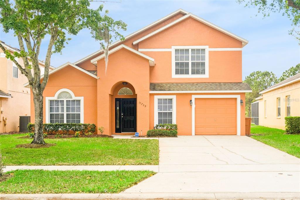 A two-story, orange-stucco suburban house features a front-facing garage and a covered entryway — 17729 WOODCREST WAY, CLERMONT, FL
