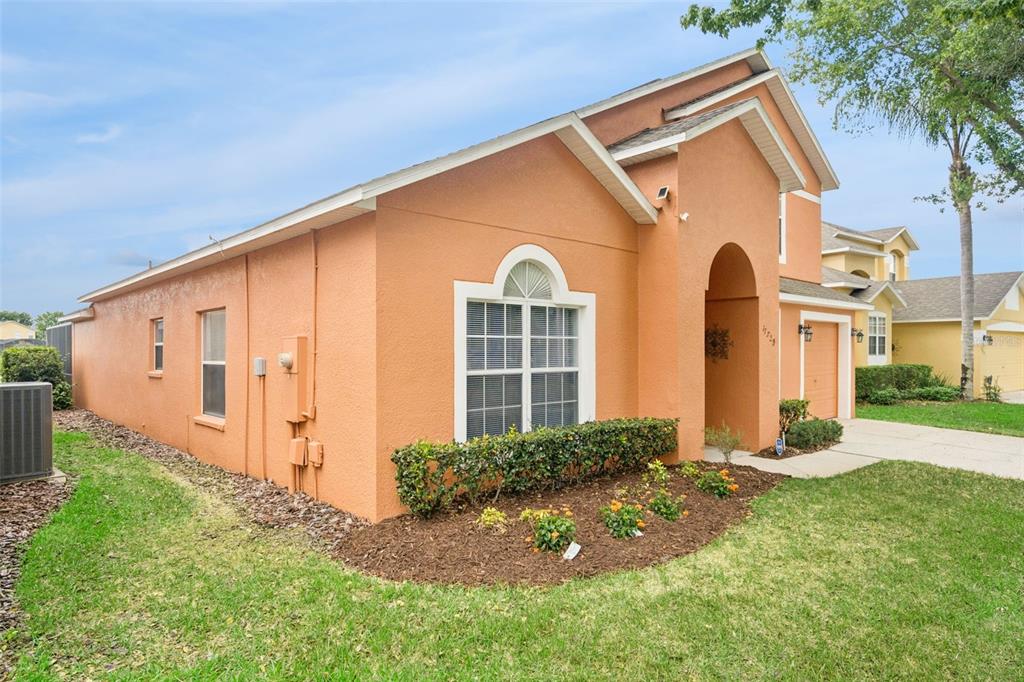 A single-story orange stucco house with a front-facing arched entryway and a landscaped garden bed — 17729 WOODCREST WAY, CLERMONT, FL