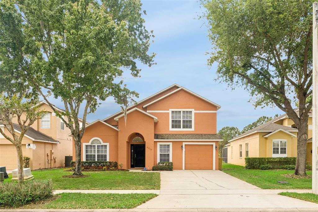 A two-story orange stucco house with a driveway, a one-car garage, and mature trees — 17729 WOODCREST WAY, CLERMONT, FL