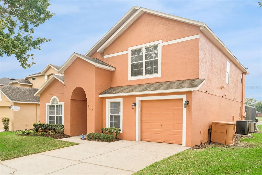 A two-story, peach-colored stucco house with a single-car garage and a concrete driveway — 17729 WOODCREST WAY, CLERMONT, FL
