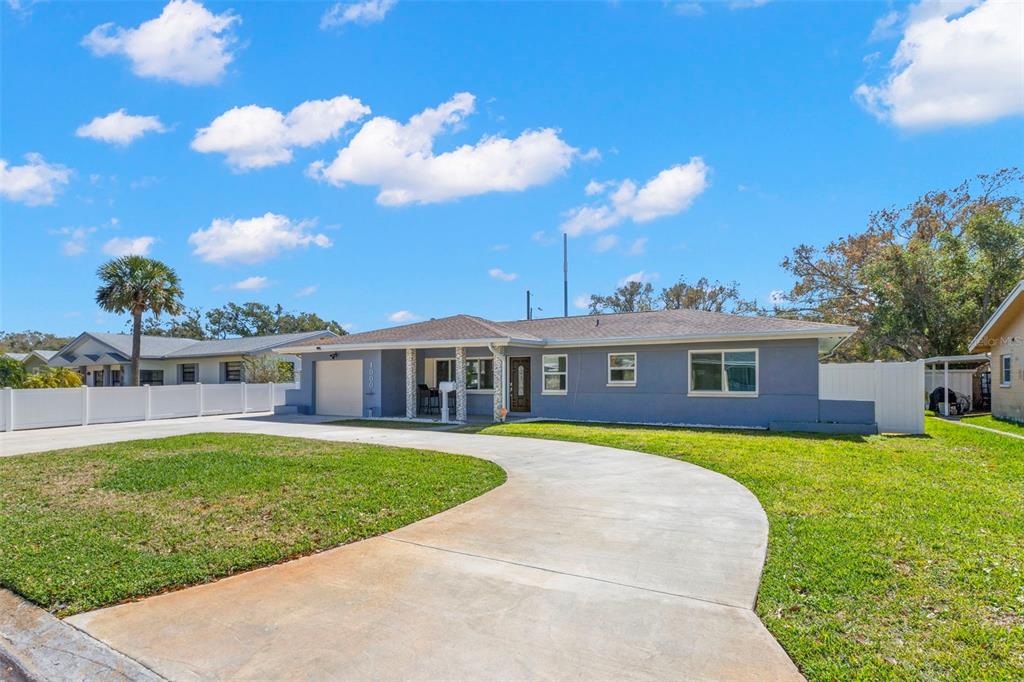A single-story gray house with a concrete driveway and a white fence under a blue sky — 1000 59TH AVENUE S, ST PETERSBURG, FL