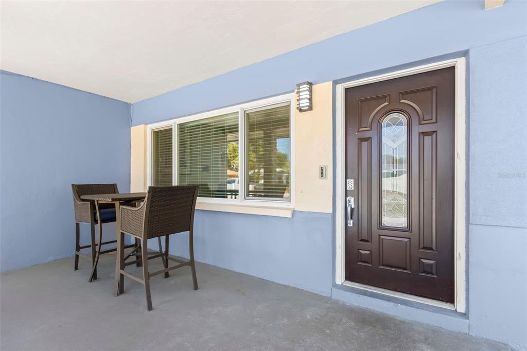 A covered porch features a brown front door, a large window, and a small table set — 1000 59TH AVENUE S, ST PETERSBURG, FL