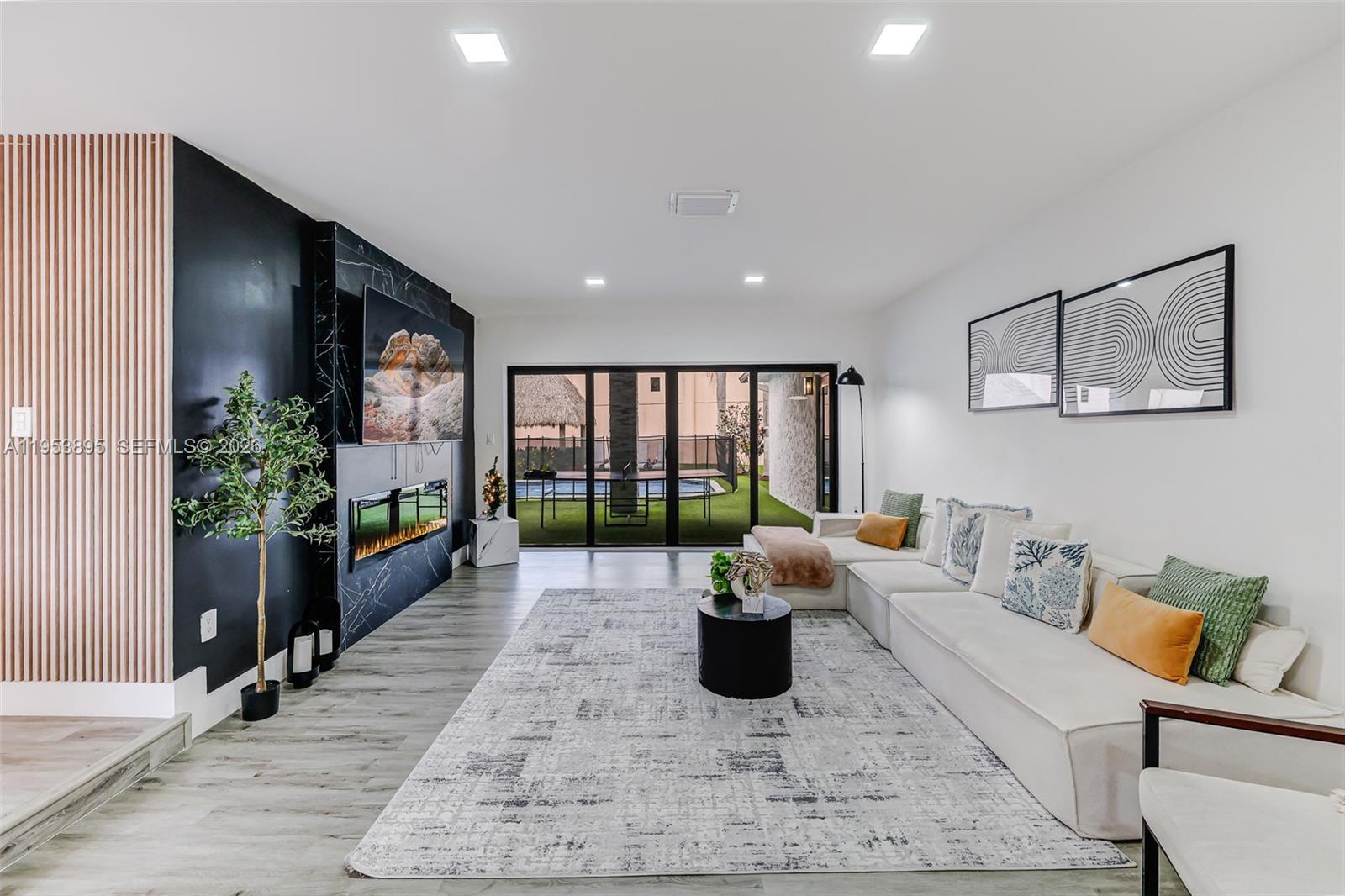 A modern living room features a black marble fireplace, white sectional sofa, and sliding glass doors — 10870 SW 106th Ave, Miami FL 33176, MIAMI, FL