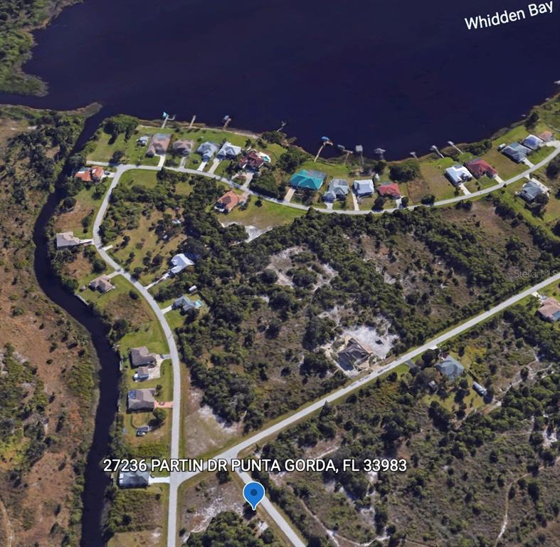 This aerial view shows a residential neighborhood with houses situated along a bay and canal — Triple Lot TITUS TERRACE, PUNTA GORDA, FL