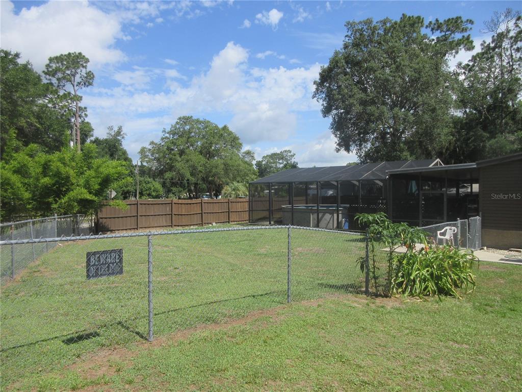 A fenced backyard features a grass lawn, a screened-in pool enclosure, and mature trees — 2300 SE 173RD AVENUE, SILVER SPRINGS, FL