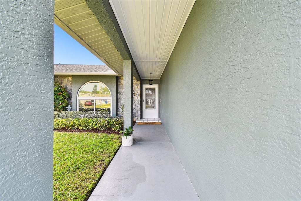 A covered concrete walkway leads to the front entrance of a house with stone siding — 4636 WHITETAIL LANE, NEW PORT RICHEY, FL