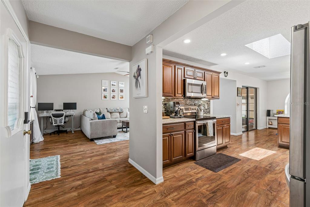 A kitchen with wood cabinets and stainless steel appliances opens into a living room area — 4636 WHITETAIL LANE, NEW PORT RICHEY, FL