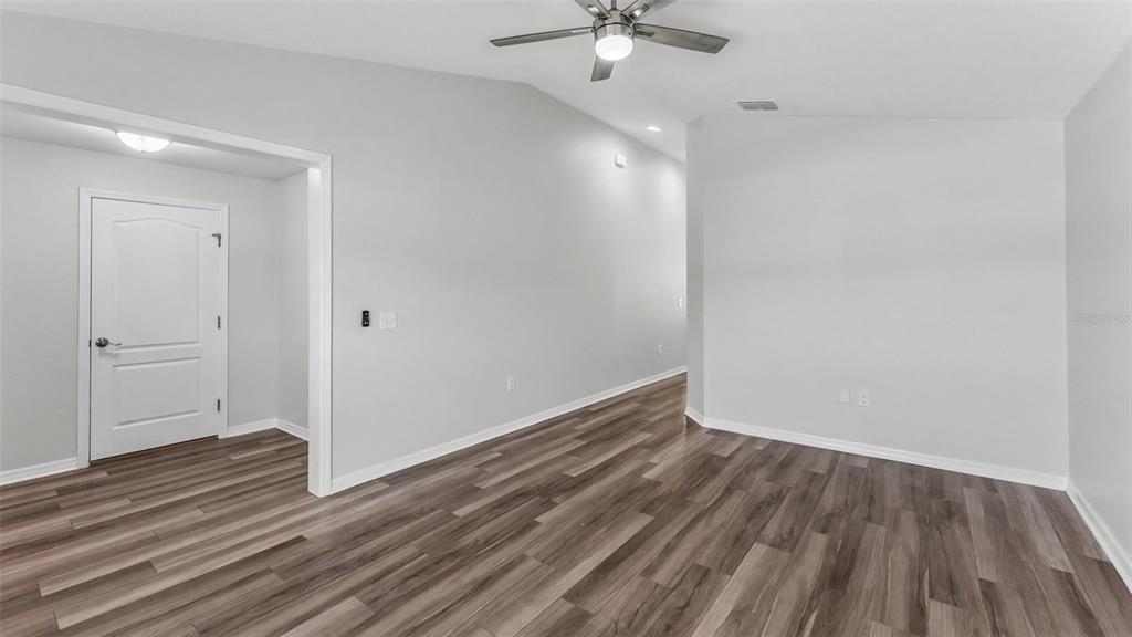An empty room features wood-look flooring, a vaulted ceiling with a fan, and a doorway — 1268 PINTAIL PLACE, LAKELAND, FL