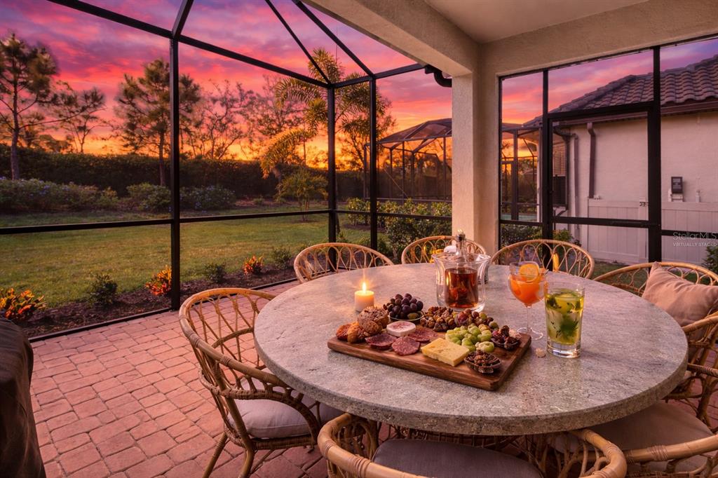A screened-in patio features a round stone table with a charcuterie board and sunset views — 14655 DERNA TERRACE, BRADENTON, FL