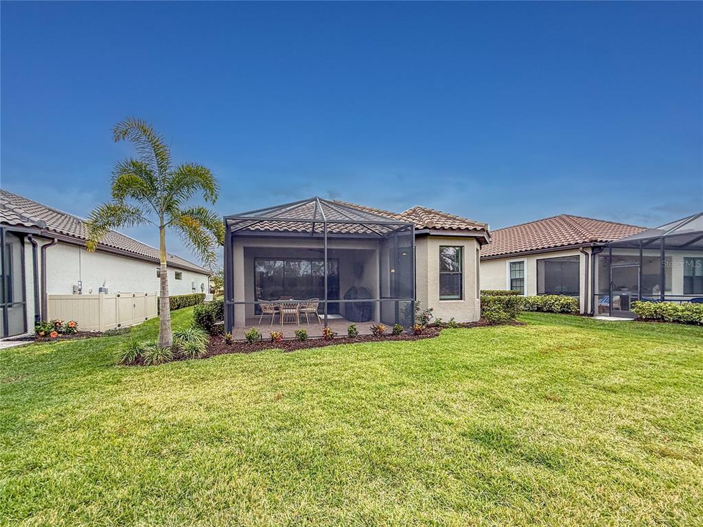 A backyard view of a house with a screened-in patio, palm tree, and lawn — 14655 DERNA TERRACE, BRADENTON, FL