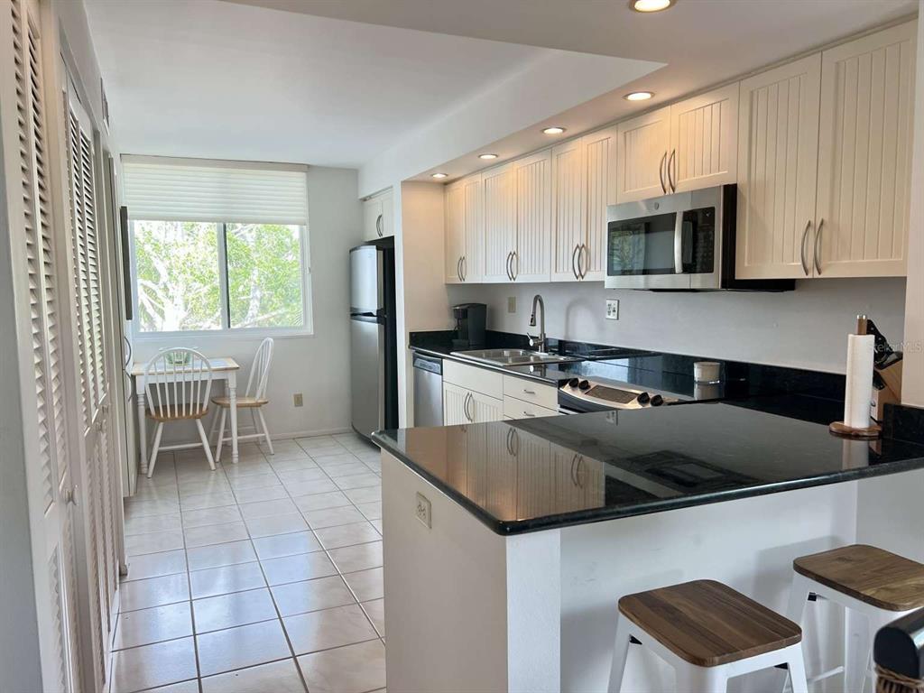 A kitchen features white cabinets, black countertops, a stainless steel microwave, and a dining area — 843 BAYPORT WAY UNIT 843, LONGBOAT KEY, FL