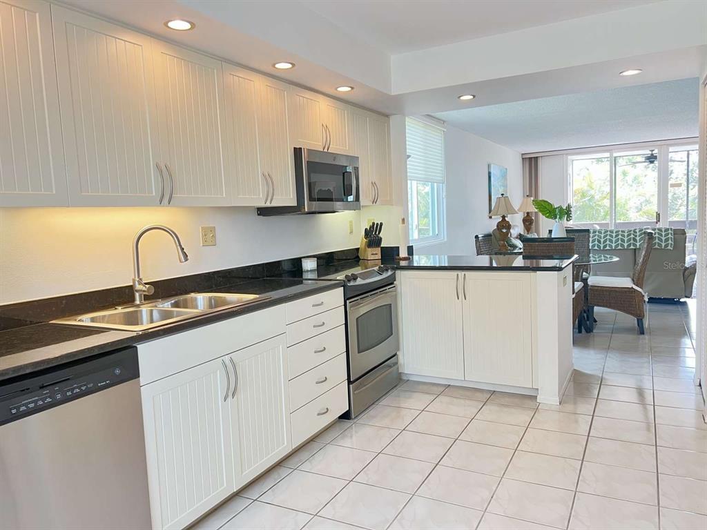 A kitchen with white cabinets, black countertops, and stainless steel appliances opens to a living area — 843 BAYPORT WAY UNIT 843, LONGBOAT KEY, FL