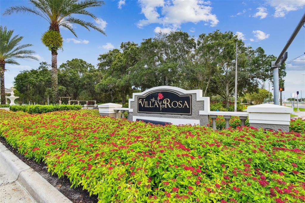 A sign for Villa Rosa sits behind a large bed of red flowers and greenery — 19108 CENTRE ROSE BOULEVARD, LUTZ, FL