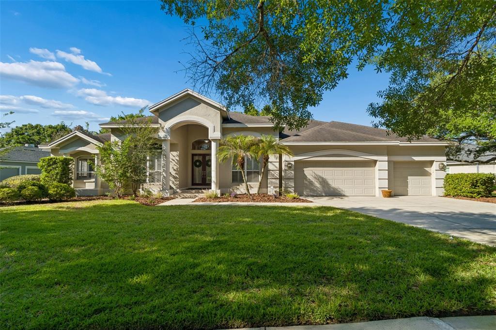 A single-story suburban house with a beige stucco exterior, a three-car garage, and a lawn — 19108 CENTRE ROSE BOULEVARD, LUTZ, FL