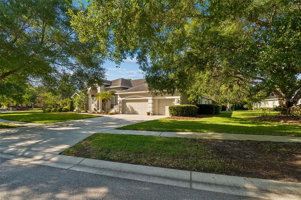 A single-story house with a three-car garage sits on a grassy lot under large trees — 19108 CENTRE ROSE BOULEVARD, LUTZ, FL