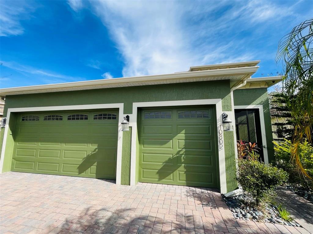 A two-car garage with green doors and a paver driveway under a blue sky — 10802 WILLOW RIDGE LOOP, ORLANDO, FL