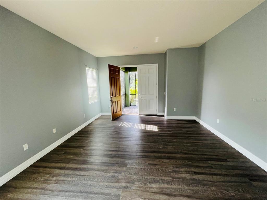 An empty room with gray walls, dark wood-look flooring, and an open door to a porch — 10802 WILLOW RIDGE LOOP, ORLANDO, FL