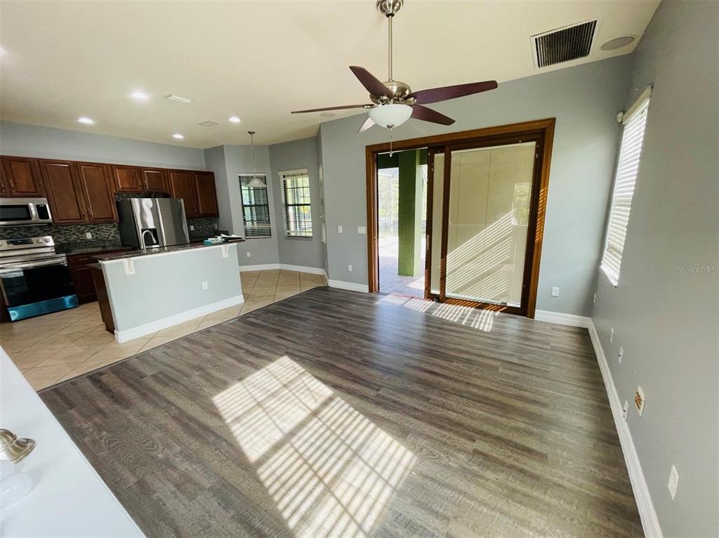 An open-concept living area with wood-look flooring connects to a kitchen with dark cabinetry — 10802 WILLOW RIDGE LOOP, ORLANDO, FL
