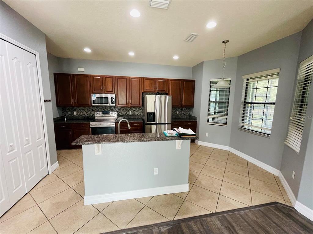 A kitchen features dark wood cabinets, granite countertops, a center island, and tile flooring — 10802 WILLOW RIDGE LOOP, ORLANDO, FL