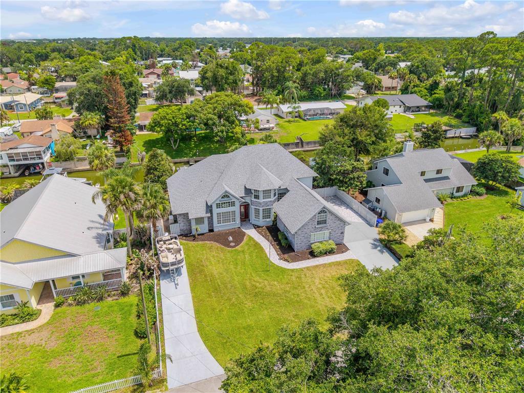 An aerial view shows a gray house with a large lawn, driveway, and canal access — 128 GODFREY ROAD, EDGEWATER, FL