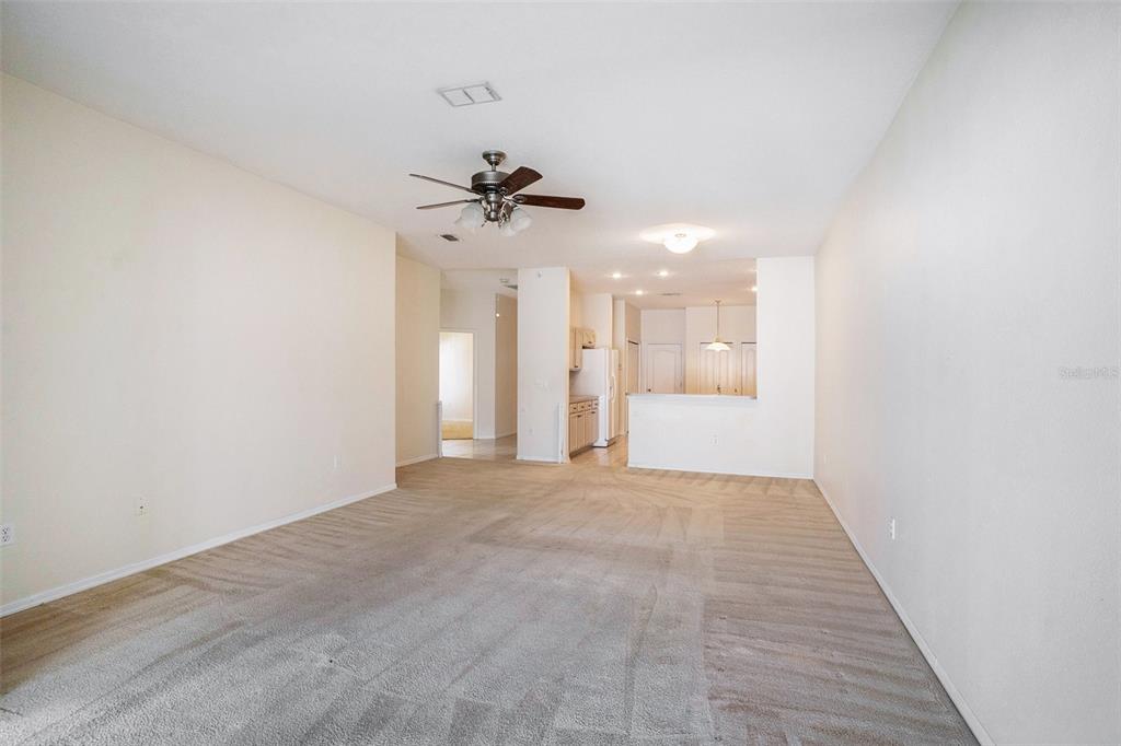 A carpeted living room opens to a kitchen with a breakfast bar and ceiling fan — 1837 RAVENRIDGE STREET, WESLEY CHAPEL, FL