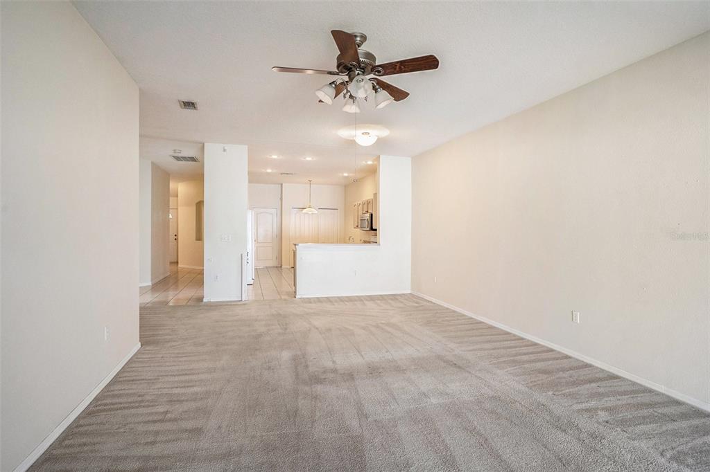 A carpeted living room opens to a kitchen with a breakfast bar and ceiling fan — 1837 RAVENRIDGE STREET, WESLEY CHAPEL, FL