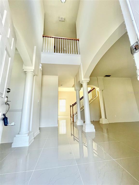 A bright entryway features white columns, tile flooring, and a staircase with a wooden railing — 2370 HINSDALE DRIVE, KISSIMMEE, FL