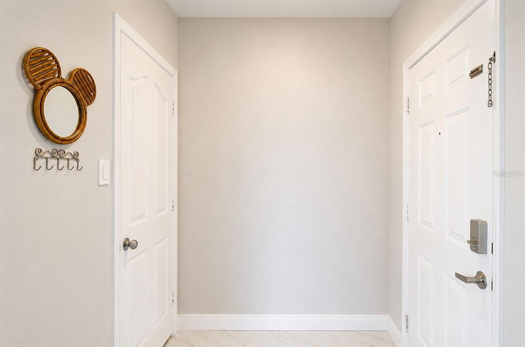 A bright entryway features a white door, a closet door, and a Mickey-shaped wall mirror — 770 SIENA PALM DRIVE UNIT 206, CELEBRATION, FL