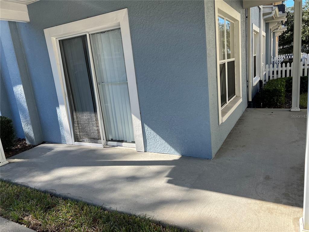 A concrete patio sits outside a blue house with a sliding glass door and window — 2280 SAN VITAL DRIVE UNIT 107, KISSIMMEE, FL