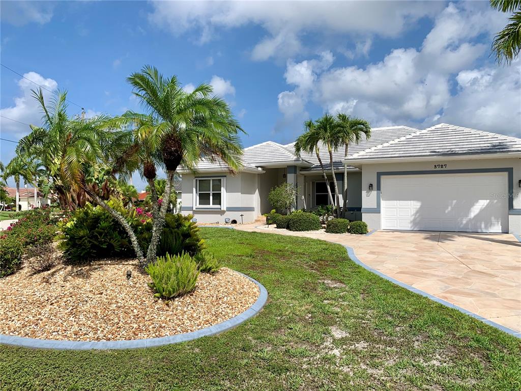 A single-story house with a white garage, a paved driveway, and palm trees in front — 3727 WHIPPOORWILL COURT, PUNTA GORDA, FL