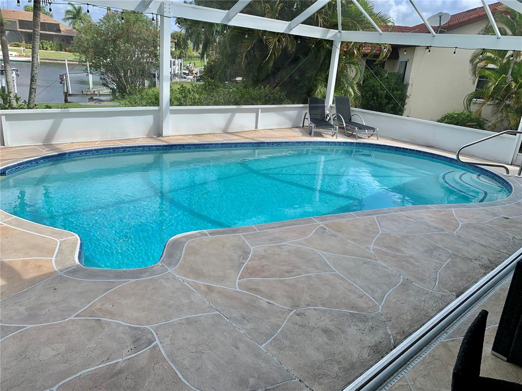 A screened-in swimming pool with a concrete deck overlooks a canal and neighboring homes — 3727 WHIPPOORWILL COURT, PUNTA GORDA, FL