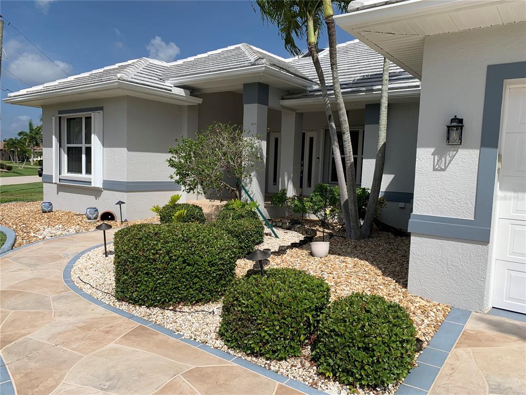 The exterior of a house features a stone walkway, manicured shrubs, and palm trees — 3727 WHIPPOORWILL COURT, PUNTA GORDA, FL
