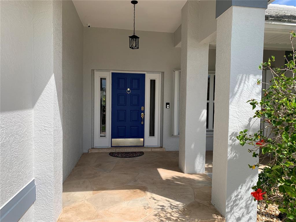 A covered entryway features a blue front door with sidelights and stone flooring — 3727 WHIPPOORWILL COURT, PUNTA GORDA, FL
