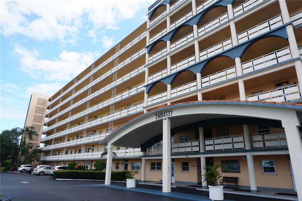 The exterior of a multi-story apartment building features a covered entrance and blue arched accents — 5900 SHORE BOULEVARD S UNIT 402, GULFPORT, FL