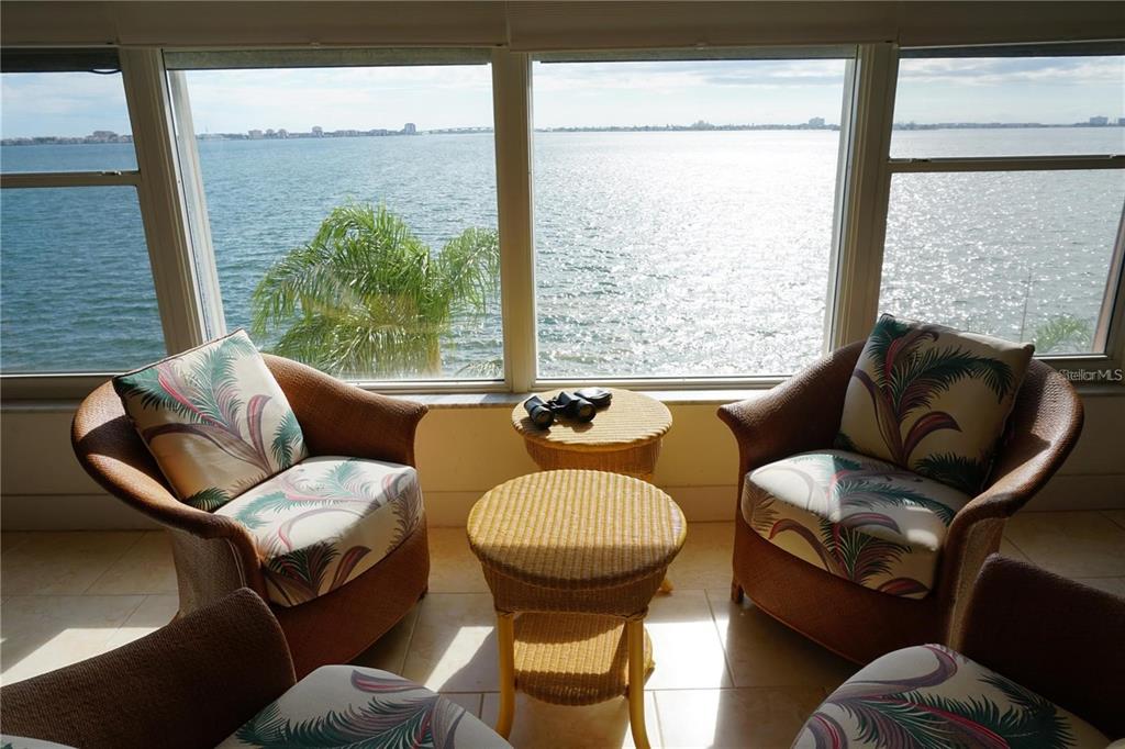 Three wicker chairs with tropical cushions face a large window overlooking a wide bay — 5900 SHORE BOULEVARD S UNIT 402, GULFPORT, FL
