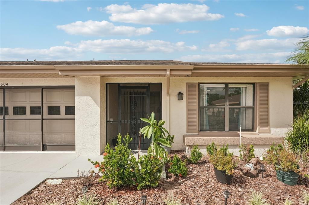 The exterior of a single-story home features a garage, a screened entryway, and landscaping — 1604 LELAND DRIVE, SUN CITY CENTER, FL