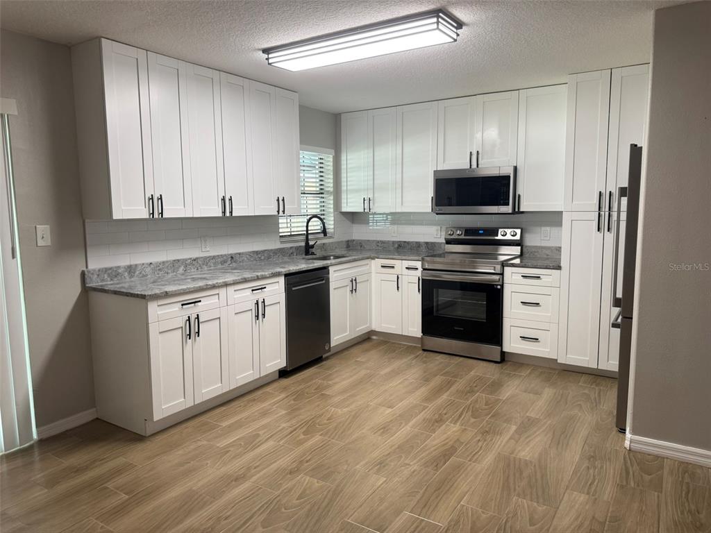 A kitchen features white shaker cabinets, stainless steel appliances, gray countertops, and wood-look tile flooring — 1008 N BRACEWELL DRIVE, PLANT CITY, FL